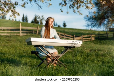 Girl playing a synthesizer piano in nature at sunset. A woman is 22 years old. An electric piano stands in a field in a village. Spring day in the countryside. 