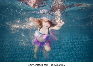 Girl playing underwater in the pool floats and spins among the air bubbles. Healthy family lifestyle and children water sports activity. Child development, disease prevention  