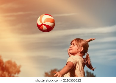 A girl is playing volleyball . The child hits the ball with his hand . Outdoor play - Powered by Shutterstock