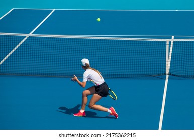 A girl plays tennis on a court with a hard blue surface on a summer sunny day - Powered by Shutterstock