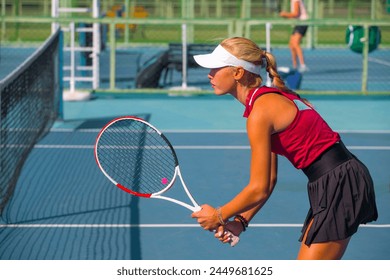 A girl plays tennis on a court with a hard blue surface on a summer sunny day - Powered by Shutterstock