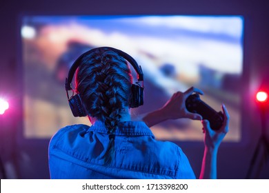 Girl Plays A Video Game On The Big TV Screen In The Dark Room. Gamer With A Joystick. Online Gaming With Friends At Night, Competitions, Win, Prize. Fun Entertainment. Teens Play Adventure Games