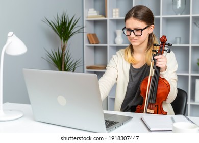 A Girl Plays The Violin Remotely Online Looking Into A Laptop. Music Lesson At Home By Video Call.