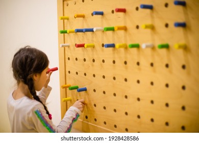 The Girl Plays With Wooden Pegboard With Round Pegs