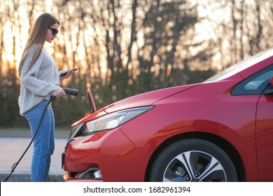 Girl stopft Elektrofahrzeug für die Ladung von Autobatterien auf dem Parkplatz. Elektrofahrzeug mit angeschlossenem Ladekabel. EV-Parkplatz, Ladekabel, Ladestation.