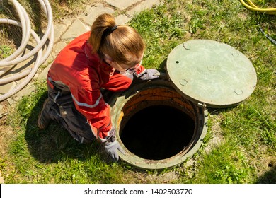 Girl plumber looks into an open draining manhole. Service of the house individual sewerage.