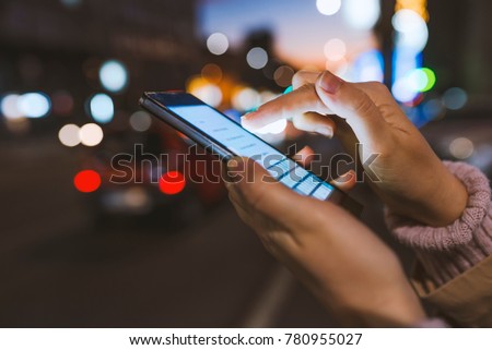Girl pointing finger on screen smartphone on background illumination bokeh color light in night atmospheric city, using in hands texting mobile phone. Using cellphone at night