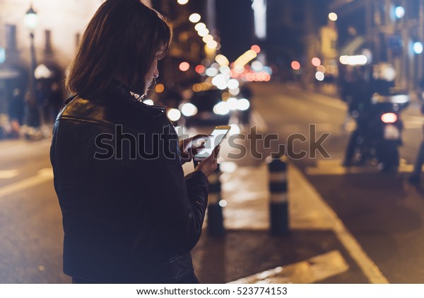 Girl pointing finger on screen smartphone on\
background illumination glow bokeh light in night atmospheric\
christmas city, hipster using mobile phone, headlights auto taxi;\
mockup glitter street