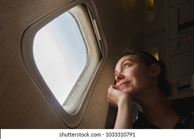 Girl at the porthole in the plane. Young woman on passenger seat near window in airplane