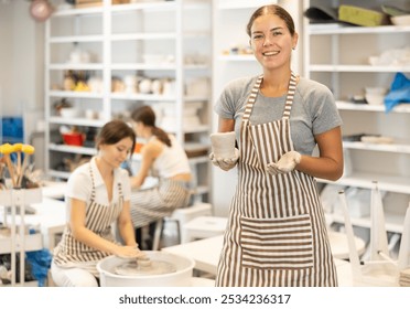 Girl in pottery workshop got her hands dirty in clay solution in process of working, having fun and rejoicing at successful training during master class and meeting with like-minded people - Powered by Shutterstock