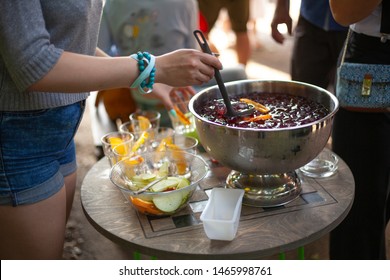 The Girl Pours A Punch Into A Glass. Bowl With A Light Alcoholic Drink At A Party. Holiday Outdoors With Delicious Drinks. Treats For Guests.