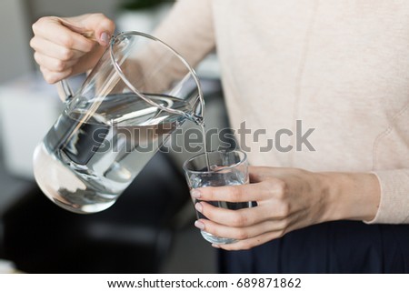 A girl pours water from a decanter into a glass. Close up. 