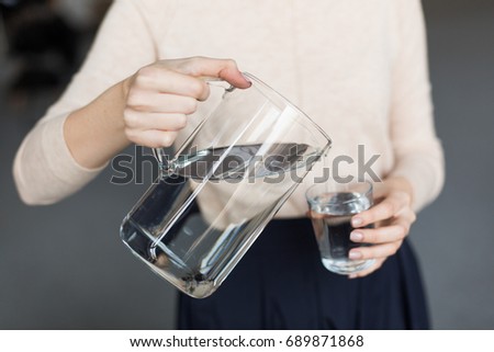A girl pours water from a decanter into a glass. Close up. 