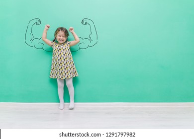 Girl power. The child with hand-drawn muscles in his arms.Funny little girl on a turquoise background with a place for text.