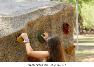 Girl practicing rock climbing on an artificial wall in a playground, developing strength and coordination - Powered by Shutterstock