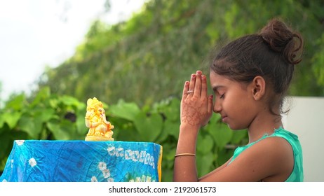 Girl Praying With Eyes Closed And Folded Hands In Front Of An Idol Of Lord Ganesha During Ganesha Or Vinayaka Chaturthi Festival Celebrations At Home - Delhi, India, August, 2022
