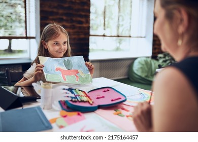 Girl presenting her artwork teacher  Woman assisting schoolgirl during classes at primary school  Child drawing picture sitting at desk in classroom  Girl drawing pictures  Learning at primary school