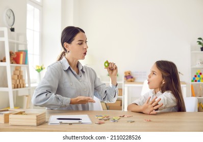Girl of primary school age practices correct pronunciation with female speech therapist. Child learns alphabet and performs exercises to correct language deficiencies. Children speech therapy concept.