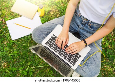 Girl Prints On A Laptop, Top View. Remote Learning, Watching A Lesson In The Park On The Lawn. Do Your Homework And Work Outside The Home.