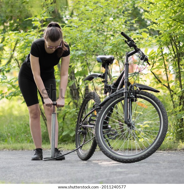 A girl pumps a bicycle wheel with a\
pump. Bicycle repair in the forest. Close\
up.