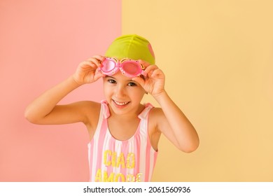 A girl puts on children's swimming goggles with a cute smile isolated on a yellow-pink studio background. Swimming training in the pool. Advertising concept.The joy of training with a swimmer - Powered by Shutterstock