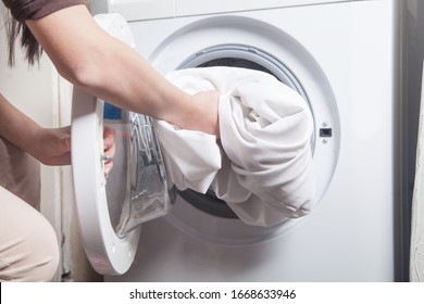 Girl Putting Bed Clothes In Washing Machine.