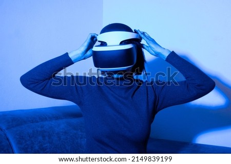 Girl putting on a vr helmet to enter the virtual universe at home in blue light. The concept of the virtual universe. Lifestyle in the virtual space