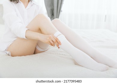 Girl Putting On White Stockings At Home. Anti-embolic Stockings. Compression Hosiery. Medical Stockings, Tights, Socks, Calves And Sleeves For Varicose Veins And Venouse Therapy.