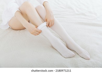 Girl Putting On White Stockings At Home. Anti-embolic Stockings. Compression Hosiery. Medical Stockings, Tights, Socks, Calves And Sleeves For Varicose Veins And Venouse Therapy.