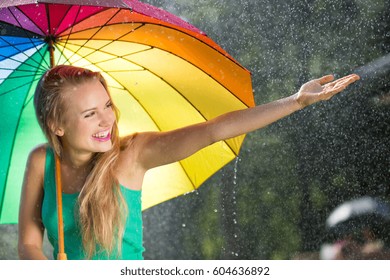 Girl with rainbow umbrella under summer rain