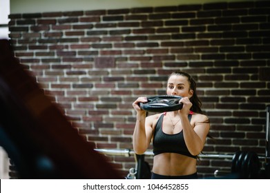 The girl raises a metal round weights plate, dumbbell in hands above her head. Portrait of strong sporty woman doing exercise in gym. sport, fitness, lifestyle.