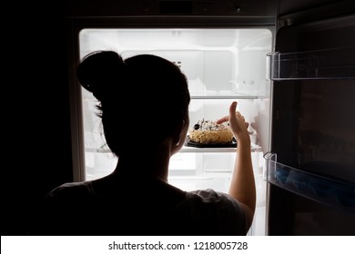 The girl reaches for harmful food in the fridge