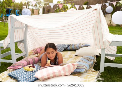 Girl Reading Book And Eating Snack In Home Made Garden Den