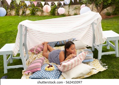 Girl Reading Book And Eating Snack In Home Made Garden Den