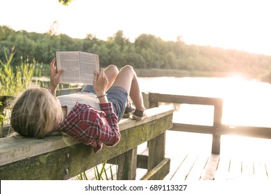 Girl Reading A Book Outside In Summer Sun At The Lake