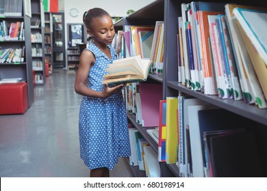 Girl reading book while standing by shelf in library - Shutterstock ID 680198914