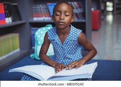 Girl reading braille book while sitting in library - Powered by Shutterstock