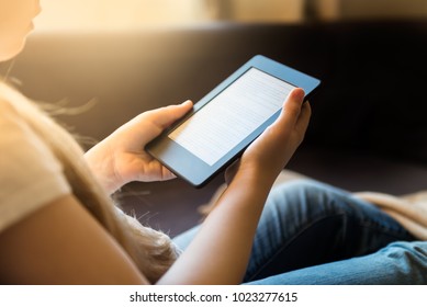 Girl is reading ebook on digital tablet device while relaxing on the sofa