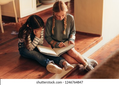 Girl reading storybook for her little sister. Two girls sitting on floor reading a book at home. - Powered by Shutterstock