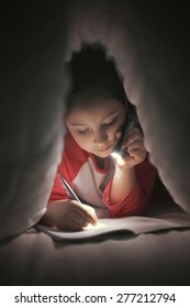 Girl reading and writing under the covers using flashlight