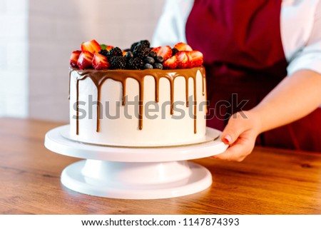 Girl in a red apron holding a birthday cake decorated with fresh berries