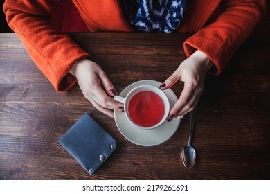 A Girl In A Red Coat In A Cafe Over A Cup Of Hot Tea, A Blue Wallet Is On The Table To Pay For A Business Lunch. Lifestyle Style, Horizontal Orientation, No Face, Top View, Copy Space