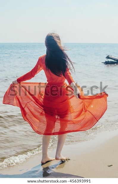 The girl in a red dress on the beach. The woman in style\
of a vamp a make-up. Power of the car and woman\'s subtlety . View\
from a back . 