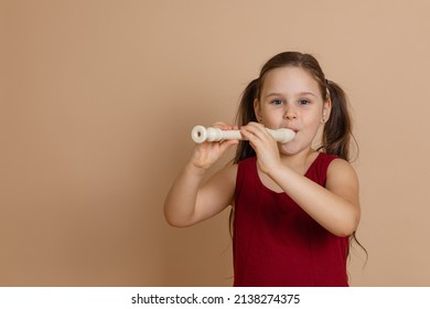 Girl in red dress play melody on flute with pleasure, blowing air into duct, beige background. Learn to play woodwind musical instrument. Flute and children is concept of music education development. - Shutterstock ID 2138274375