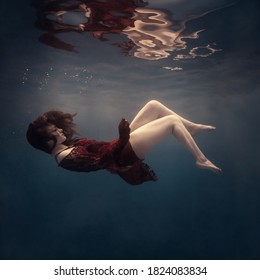 A girl in a red dress underwater with her face upside down as in weightlessness