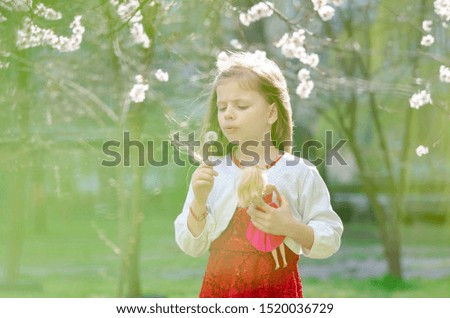 girl in a red dress and a white blouse blowing on a dandelion