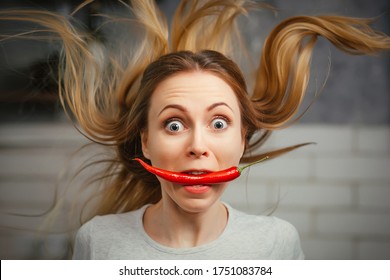 A girl with a red hot pepper in her teeth. Chili for cooking. The spicy seasoning is very stinging in the mouth. My hair stood on end. Bite the pepper and get burned. Emotional woman. - Shutterstock ID 1751083784