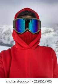 A Girl In A Red Jacket, Hat, And Ski Mask On The Background Of Mountains