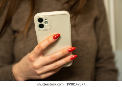 Girl With Red Long Nails In A Brown Sweater Holding A Mobile Phone