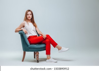 Girl In Red Pants Sitting In A Chair On A Light Gray Background